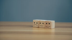 Satisfaction concept, Close up icon smiley face and blurred sad face on wood cube